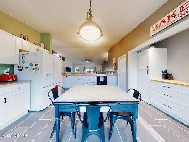 kitchen featuring ceiling fan, white appliances, white cabinetry, hanging light fixtures, and a breakfast bar area