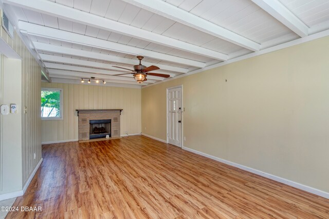 unfurnished living room with beamed ceiling, ceiling fan, light hardwood / wood-style flooring, a brick fireplace, and wooden walls