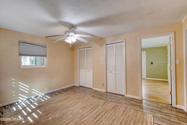 unfurnished bedroom with multiple closets, a textured ceiling, ceiling fan, and light hardwood / wood-style flooring