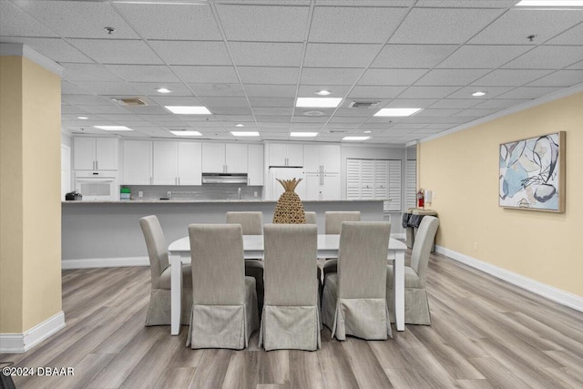 dining area with light hardwood / wood-style floors, crown molding, and a drop ceiling