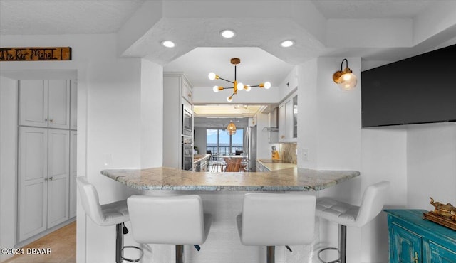 kitchen featuring kitchen peninsula, a kitchen breakfast bar, light stone countertops, an inviting chandelier, and stainless steel microwave