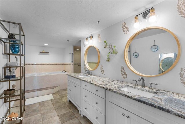 bathroom with tiled bath, vanity, a textured ceiling, and tile patterned floors