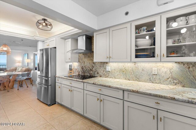 kitchen featuring tasteful backsplash, stainless steel fridge, wall chimney range hood, gray cabinets, and black electric cooktop