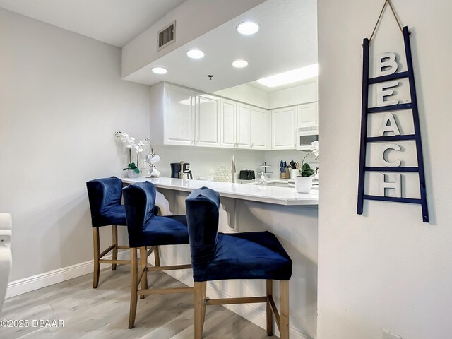 5300 S Atlantic Ave Unit 10-205, New Smyrna Beach, FL 32168 - kitchen featuring light wood-style floors, a breakfast bar area, white microwave, baseboards, and white cabinets