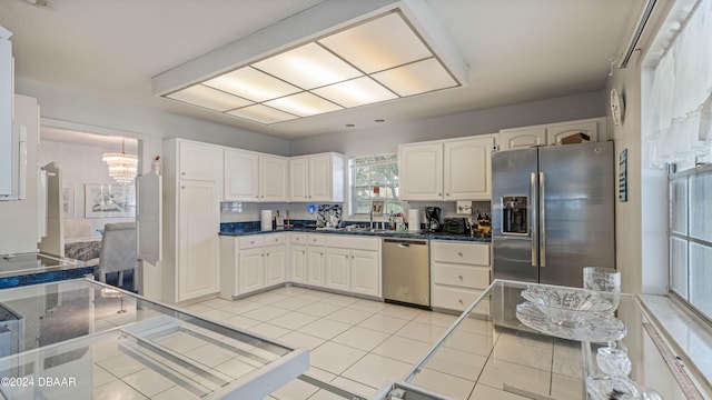 kitchen with appliances with stainless steel finishes, a notable chandelier, light tile patterned floors, sink, and white cabinets