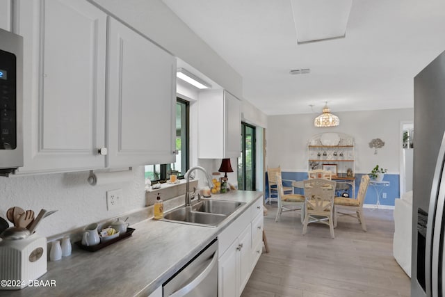 kitchen featuring sink, white cabinets, stainless steel dishwasher, a chandelier, and light hardwood / wood-style flooring