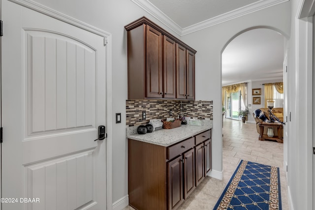 kitchen featuring dark brown cabinetry, light stone counters, decorative backsplash, and ornamental molding