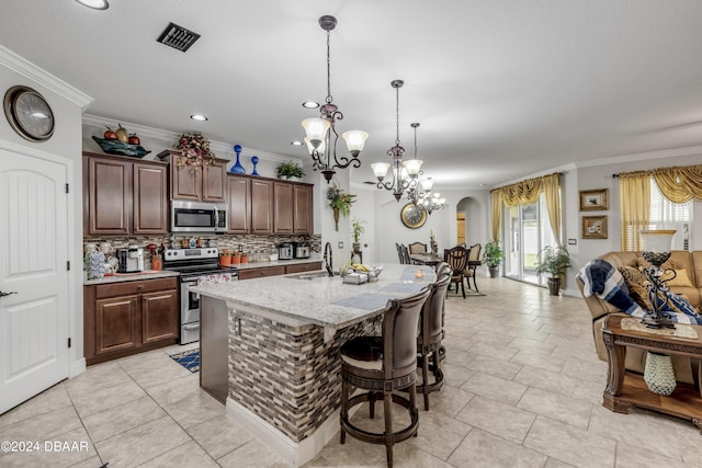 kitchen with appliances with stainless steel finishes, an island with sink, crown molding, pendant lighting, and decorative backsplash