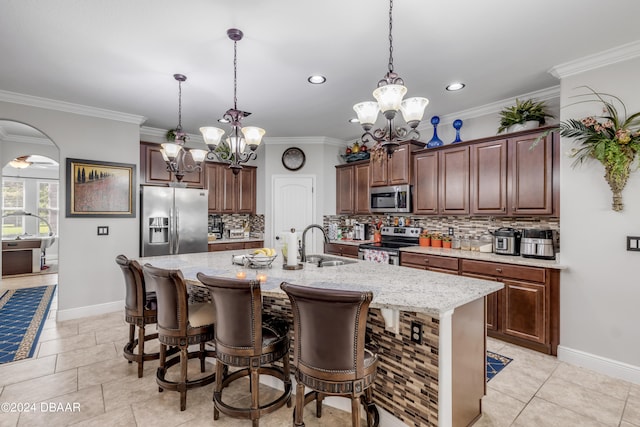 kitchen featuring stainless steel appliances, decorative backsplash, an inviting chandelier, sink, and an island with sink