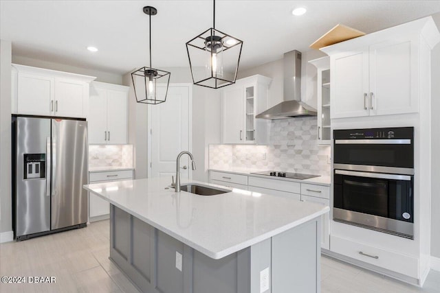 kitchen with a kitchen island with sink, wall chimney range hood, sink, white cabinetry, and stainless steel appliances