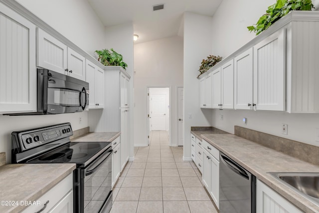 2853 Turnbull Estates Dr, New Smyrna Beach, FL 32168 - kitchen with light tile patterned flooring, white cabinets, black appliances, and high vaulted ceiling