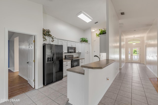 2853 Turnbull Estates Dr, New Smyrna Beach, FL 32168 - kitchen with black appliances, white cabinets, kitchen peninsula, and light tile patterned floors