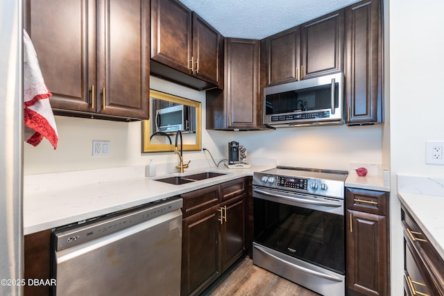 kitchen with light stone counters, sink, dark brown cabinets, and appliances with stainless steel finishes