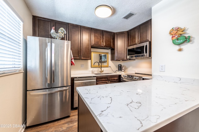 kitchen with kitchen peninsula, a textured ceiling, stainless steel appliances, sink, and dark hardwood / wood-style floors