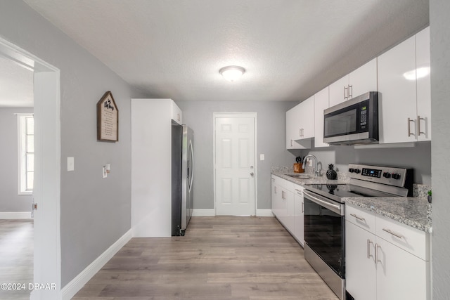 kitchen with white cabinetry, stainless steel appliances, a textured ceiling, and light hardwood / wood-style flooring