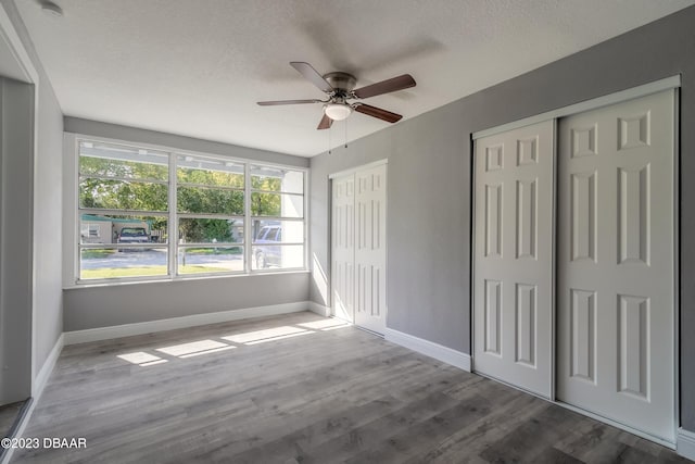 unfurnished bedroom featuring hardwood / wood-style flooring, ceiling fan, a textured ceiling, and multiple closets