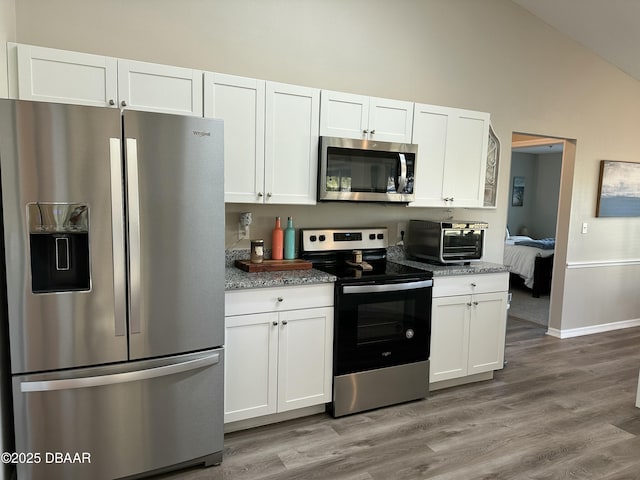 kitchen with light hardwood / wood-style flooring, vaulted ceiling, stainless steel appliances, and white cabinets