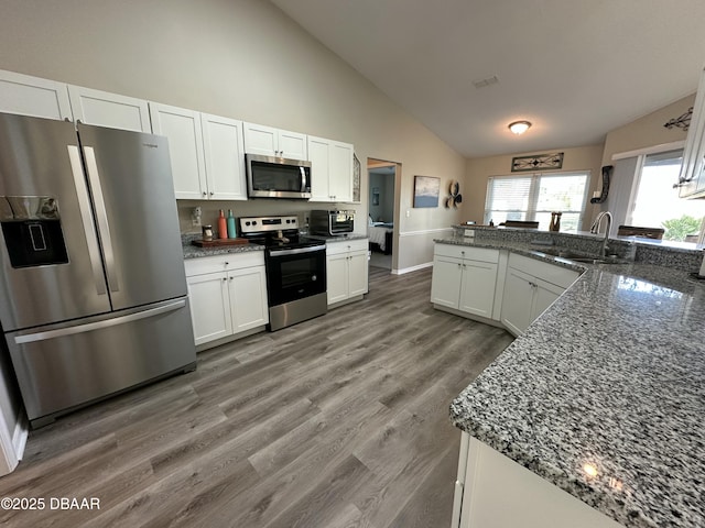 kitchen with sink, appliances with stainless steel finishes, dark stone countertops, wood-type flooring, and white cabinets