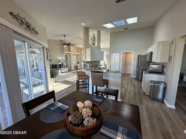 dining area with hardwood / wood-style floors, a skylight, high vaulted ceiling, and ceiling fan