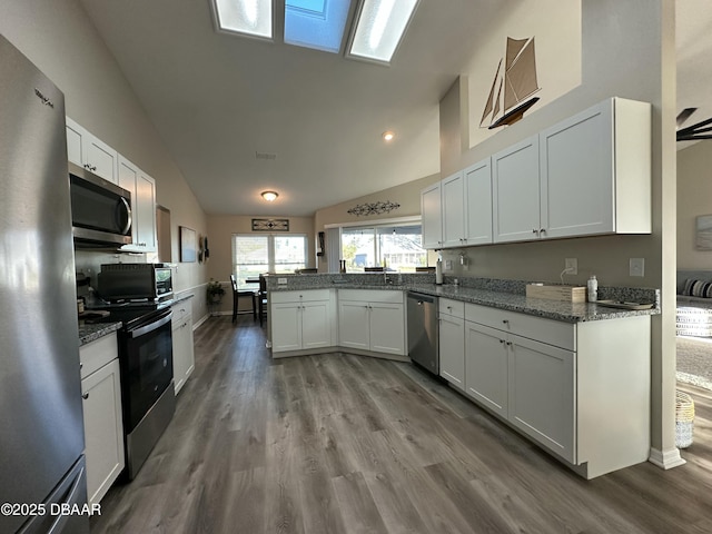 kitchen with dark stone countertops, stainless steel appliances, kitchen peninsula, and white cabinets