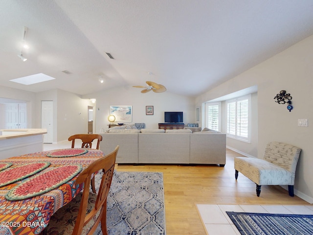 living room featuring ceiling fan, light hardwood / wood-style flooring, and vaulted ceiling with skylight