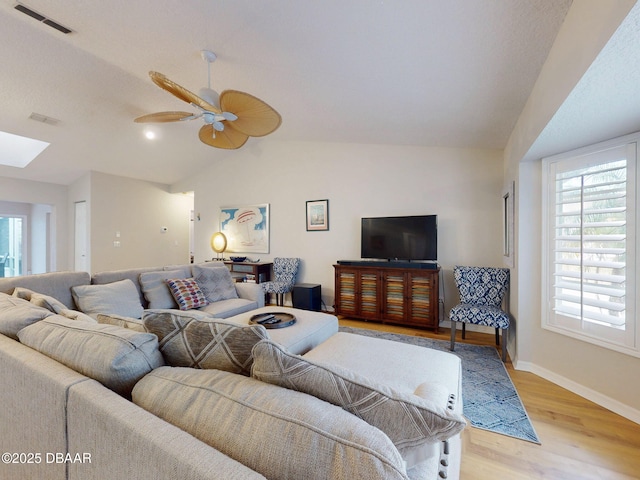 living room featuring plenty of natural light, light hardwood / wood-style floors, and vaulted ceiling with skylight