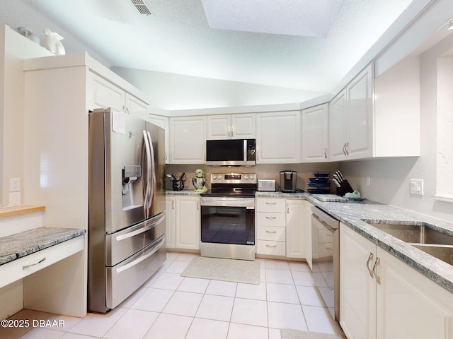 kitchen featuring light tile patterned floors, stainless steel appliances, light stone counters, white cabinets, and vaulted ceiling