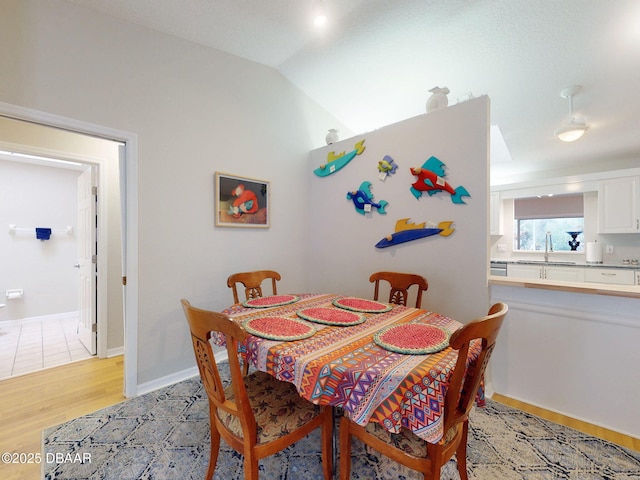 dining space with lofted ceiling, sink, and light hardwood / wood-style flooring