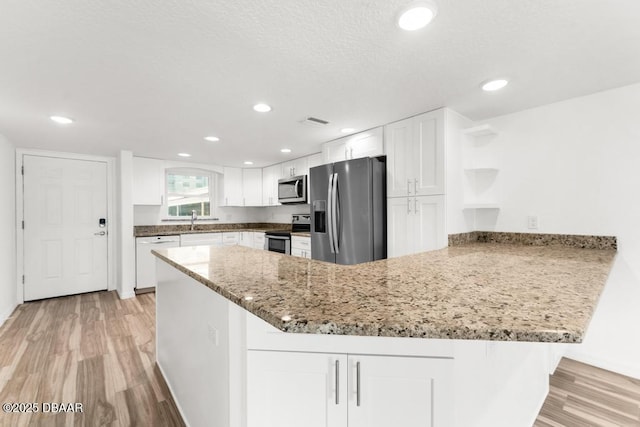 3807 S Atlantic Ave Unit 2020, Daytona Beach, FL 32118 - kitchen with stainless steel appliances, a peninsula, open shelves, light wood finished floors, and white cabinetry