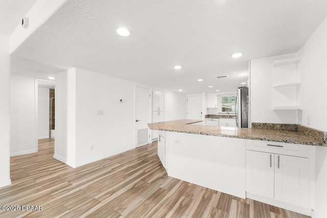 3807 S Atlantic Ave Unit 2020, Daytona Beach, FL 32118 - kitchen featuring open shelves, light wood-style floors, white cabinets, light stone countertops, and freestanding refrigerator