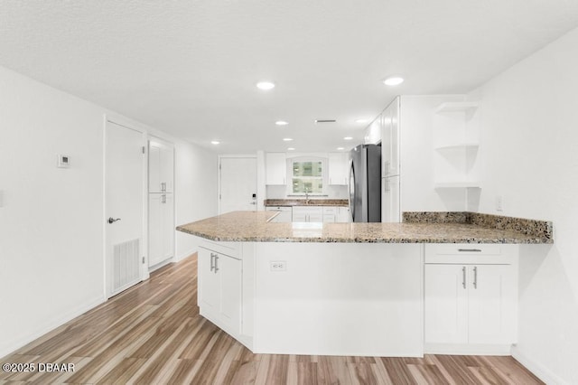 3807 S Atlantic Ave Unit 2020, Daytona Beach, FL 32118 - kitchen featuring light wood-style floors, freestanding refrigerator, a peninsula, white cabinetry, and open shelves