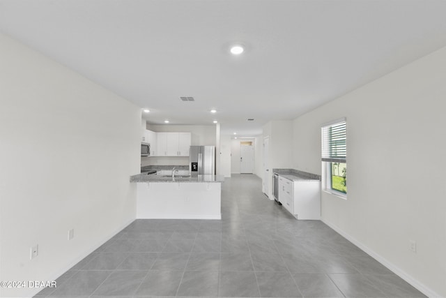 kitchen with light stone countertops, stainless steel appliances, light tile patterned floors, kitchen peninsula, and white cabinets