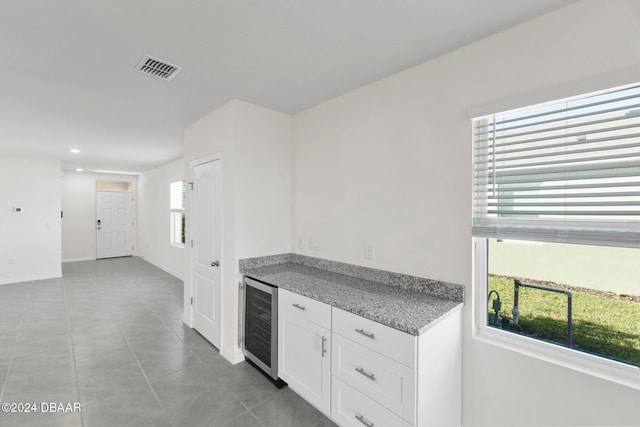 kitchen with white cabinets, a wealth of natural light, light stone counters, and beverage cooler