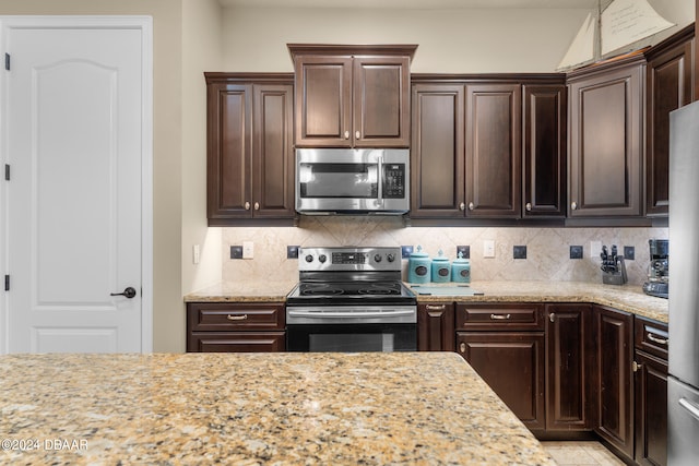 kitchen featuring light stone counters, dark brown cabinetry, stainless steel appliances, and tasteful backsplash