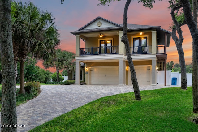 coastal inspired home with french doors, a balcony, ceiling fan, a yard, and a garage