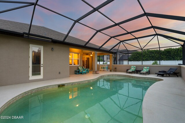 pool at dusk featuring glass enclosure, ceiling fan, and a patio area