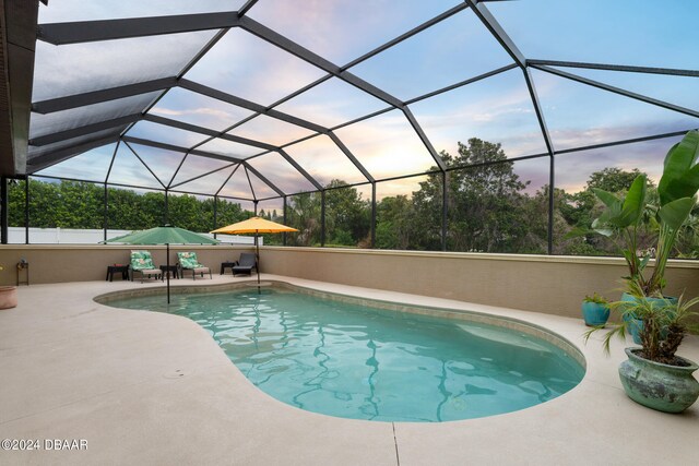 pool at dusk with glass enclosure and a patio area