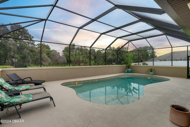 pool at dusk featuring glass enclosure and a patio