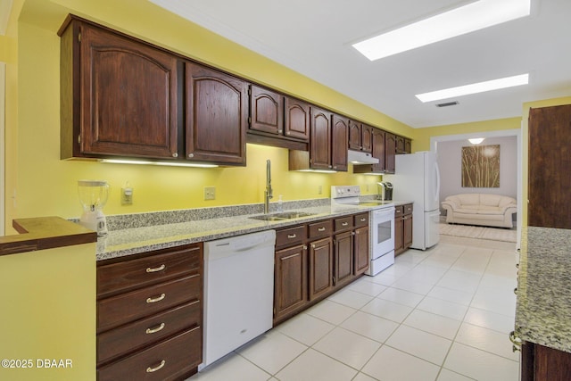 kitchen with sink, light tile patterned floors, light stone countertops, dark brown cabinets, and white appliances