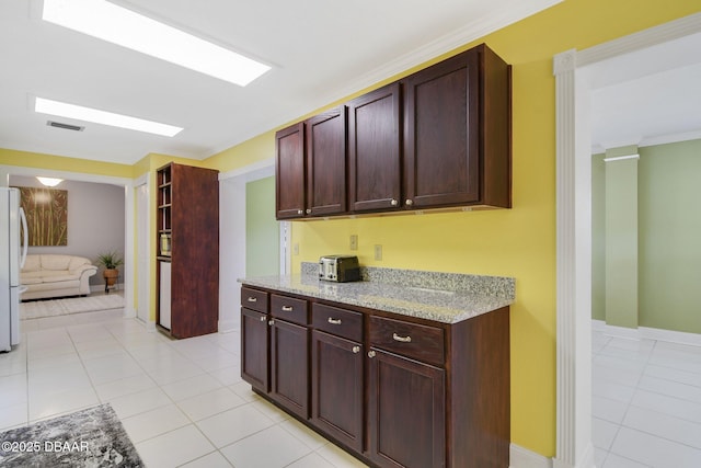 kitchen with light tile patterned floors, ornamental molding, light stone countertops, and white refrigerator