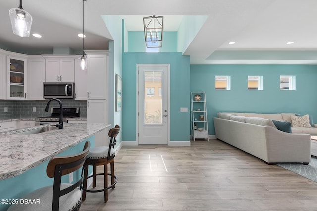 kitchen featuring pendant lighting, white cabinetry, stainless steel appliances, light stone counters, and a kitchen bar