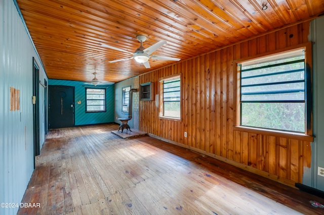 unfurnished room with wood-type flooring, wooden walls, ceiling fan, and wooden ceiling