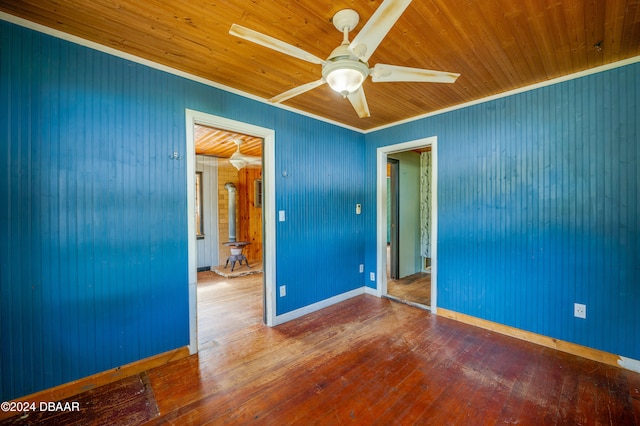 spare room with wood walls, ceiling fan, wood-type flooring, a wood stove, and crown molding