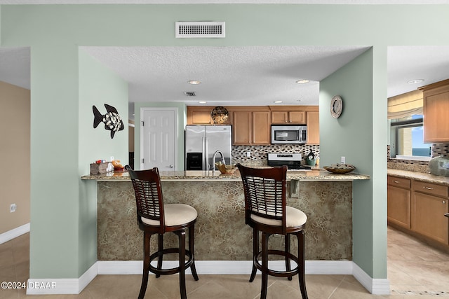 kitchen featuring a kitchen bar, appliances with stainless steel finishes, a textured ceiling, and light stone counters