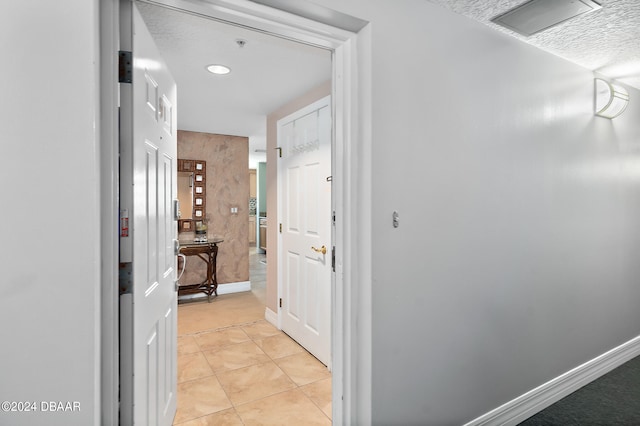 hall with a textured ceiling and light tile patterned floors