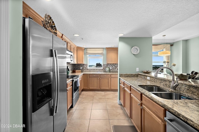 kitchen with stainless steel appliances, stone counters, sink, and decorative light fixtures