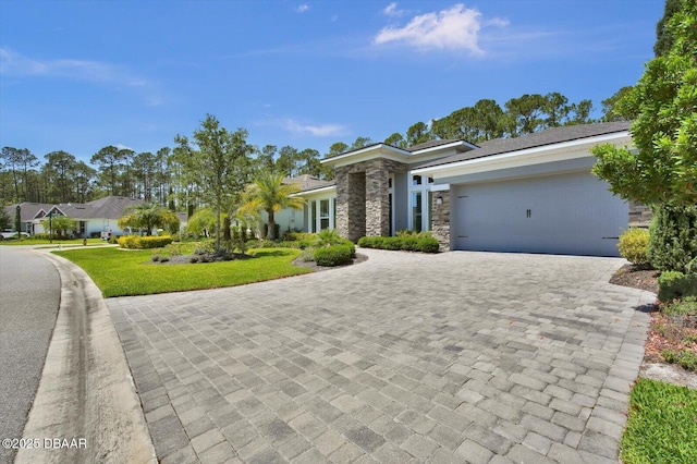 prairie-style house with decorative driveway, a front lawn, stone siding, and a garage