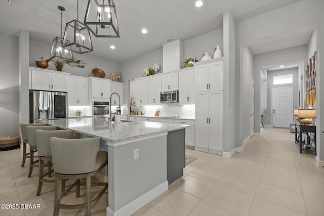 kitchen featuring appliances with stainless steel finishes, white cabinetry, decorative light fixtures, a large island with sink, and light tile patterned floors