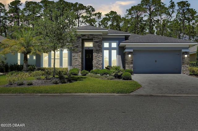 view of front facade featuring an attached garage, a front yard, driveway, and stone siding