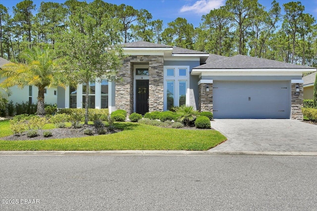 prairie-style house featuring an attached garage, stone siding, stucco siding, a front yard, and driveway